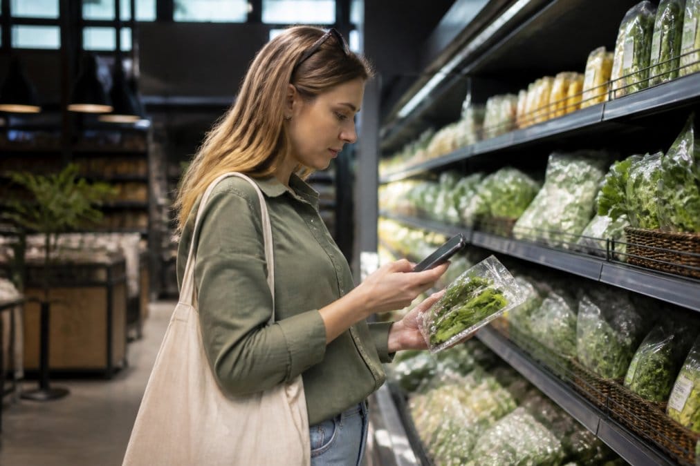 Kunde nutzt ein Smartphone im modernen Lebensmittelgeschäft als Teil vom Handel im Wandel durch digitale Preisprüfung.