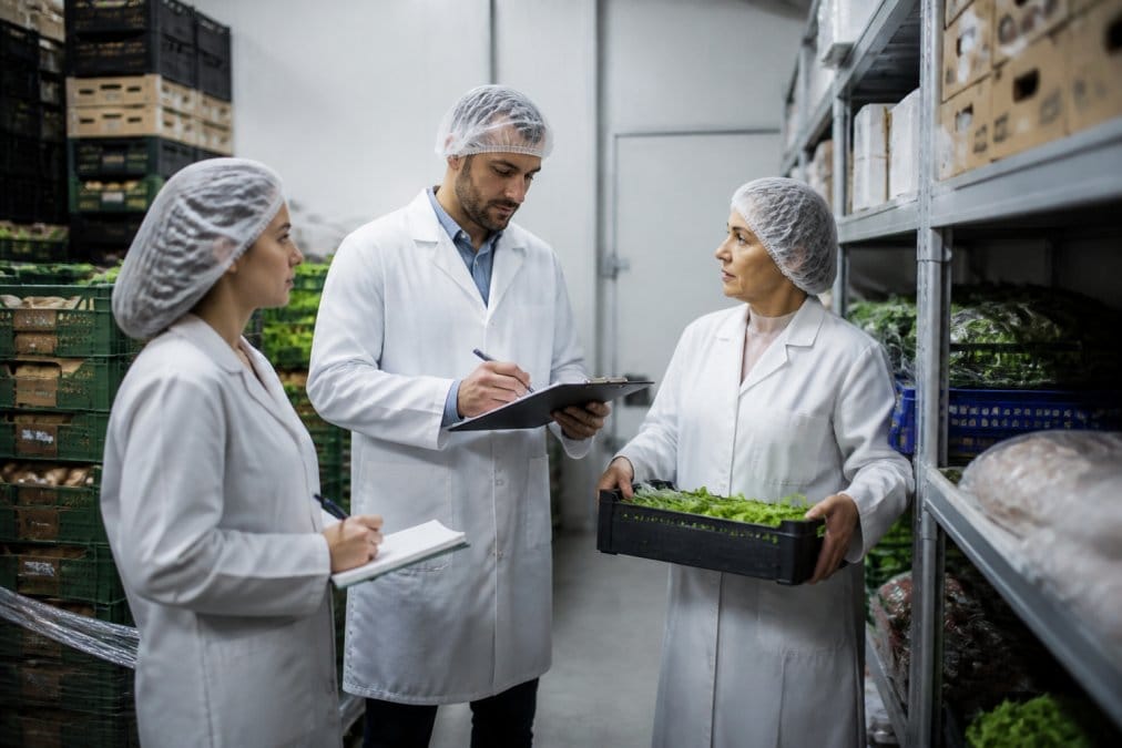 Lebensmitteleinzelhändler prüfen Lagerflächen gemäß der Hygienevorschriften Lebensmittelhandel mit Klemmbrett und Notizen.